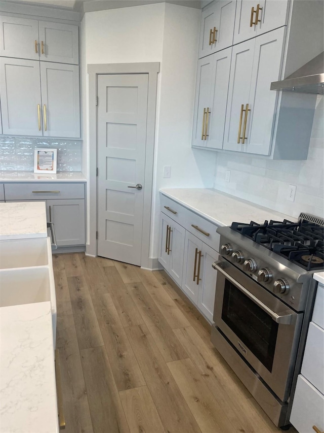 kitchen with decorative backsplash, high end stainless steel range oven, light wood finished floors, and wall chimney exhaust hood