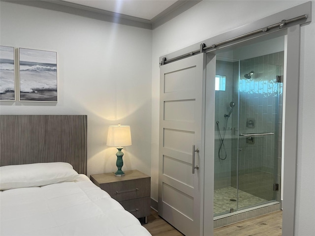 bedroom with a barn door, ornamental molding, wood finished floors, and connected bathroom