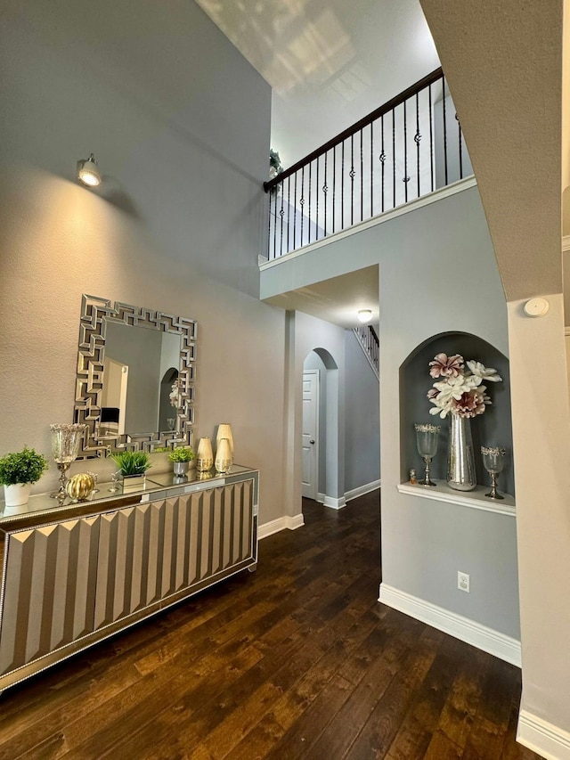 interior space with baseboards, arched walkways, a towering ceiling, and hardwood / wood-style flooring