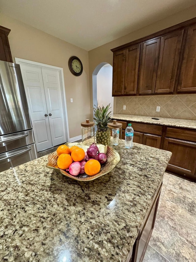 kitchen with freestanding refrigerator, arched walkways, light stone countertops, and decorative backsplash