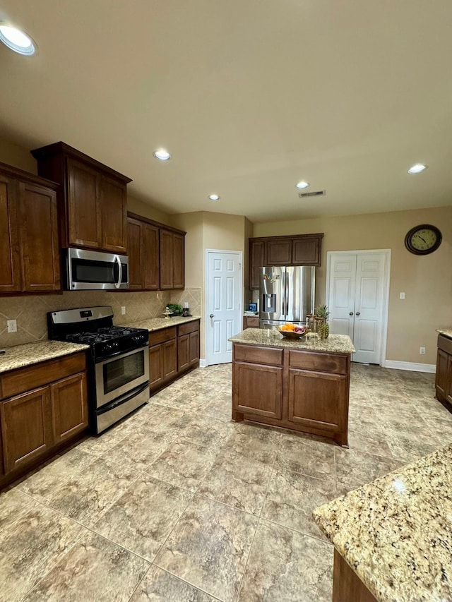 kitchen featuring visible vents, a center island, tasteful backsplash, baseboards, and stainless steel appliances