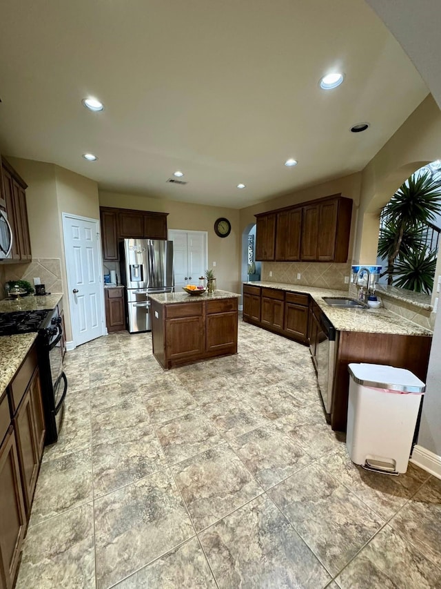 kitchen with a kitchen island, light stone countertops, a sink, appliances with stainless steel finishes, and backsplash