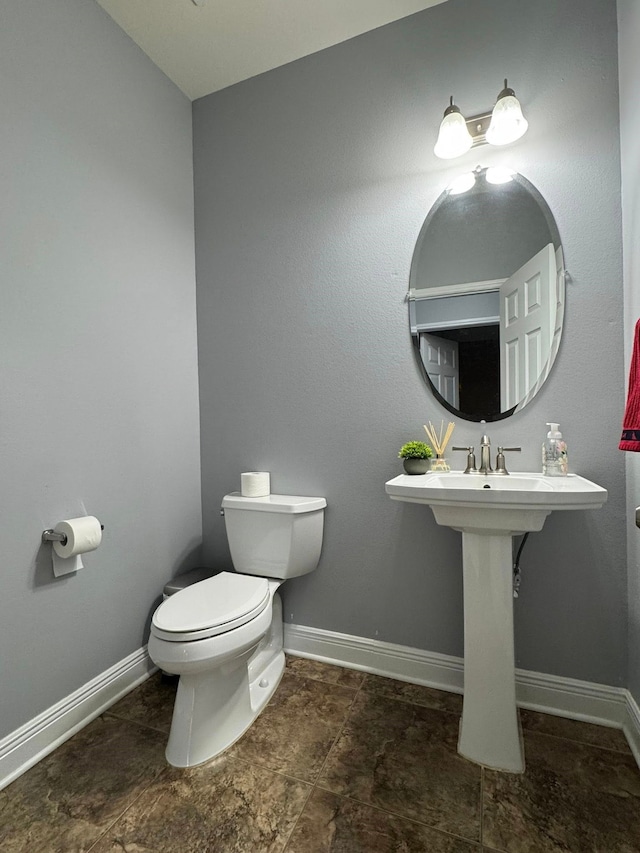 half bath featuring baseboards, toilet, and stone finish flooring
