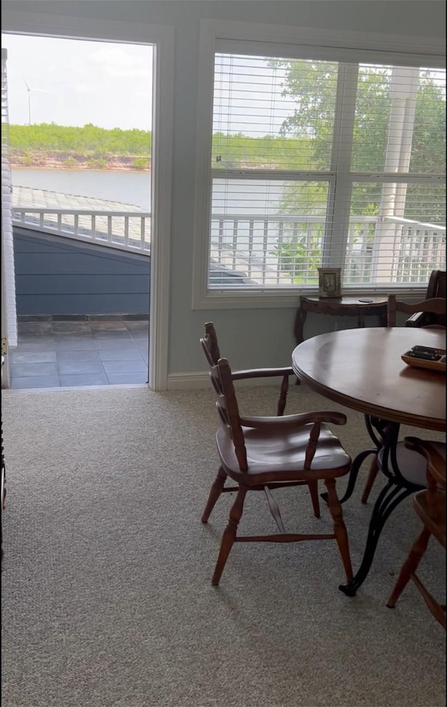 carpeted dining space with a water view and baseboards