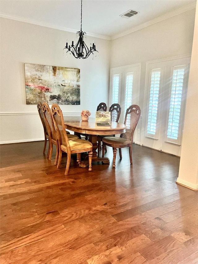 dining room featuring visible vents, wood finished floors, baseboards, a notable chandelier, and ornamental molding