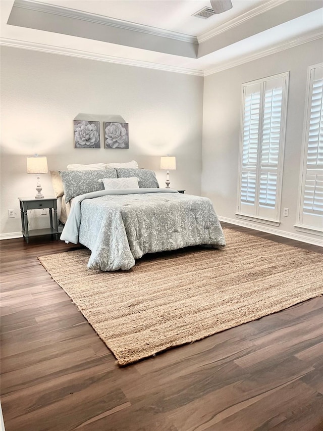 bedroom with crown molding, visible vents, wood finished floors, baseboards, and a raised ceiling