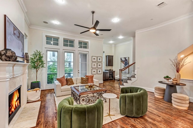 living area with ceiling fan, visible vents, a tiled fireplace, and ornamental molding