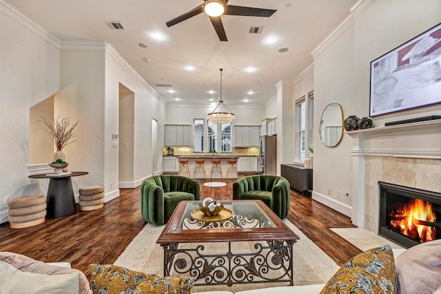 living room with crown molding, baseboards, dark wood-type flooring, a tile fireplace, and a ceiling fan