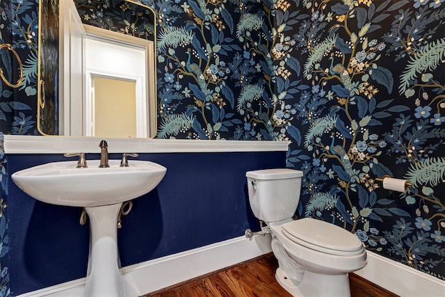half bathroom featuring toilet, wallpapered walls, and wood finished floors