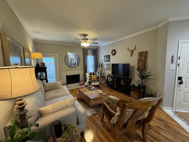 living area with a ceiling fan, a textured ceiling, ornamental molding, and wood finished floors