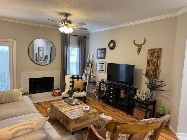 living area with a ceiling fan, a textured ceiling, crown molding, a fireplace, and wood finished floors