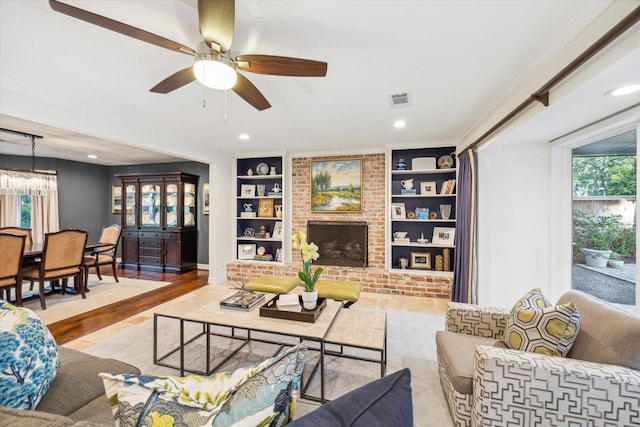 living room featuring built in shelves, ceiling fan with notable chandelier, recessed lighting, visible vents, and ornamental molding
