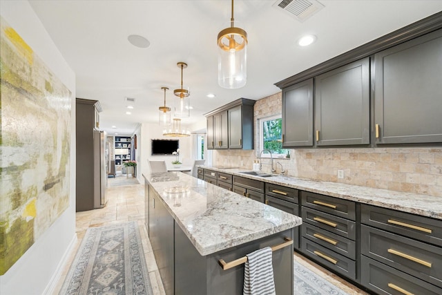 kitchen with visible vents, a center island, tasteful backsplash, light stone counters, and a sink