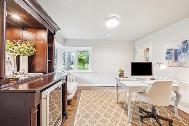 home office featuring wine cooler, baseboards, wood finished floors, and visible vents