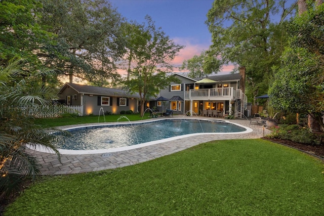 pool at dusk with fence, stairs, an outdoor pool, a patio, and a yard