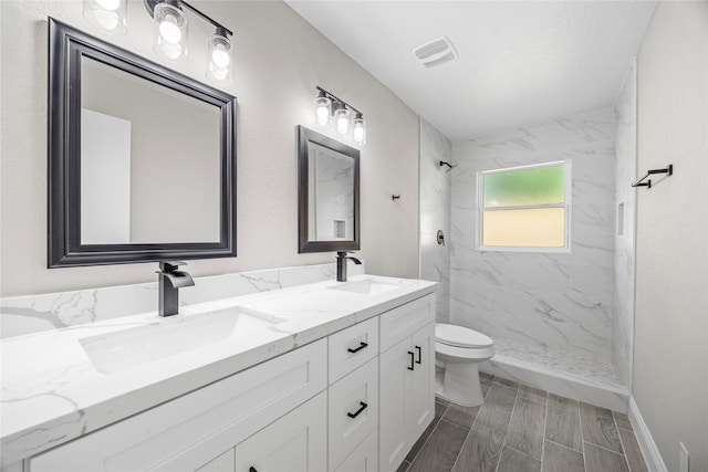 bathroom featuring double vanity, a sink, a marble finish shower, and toilet