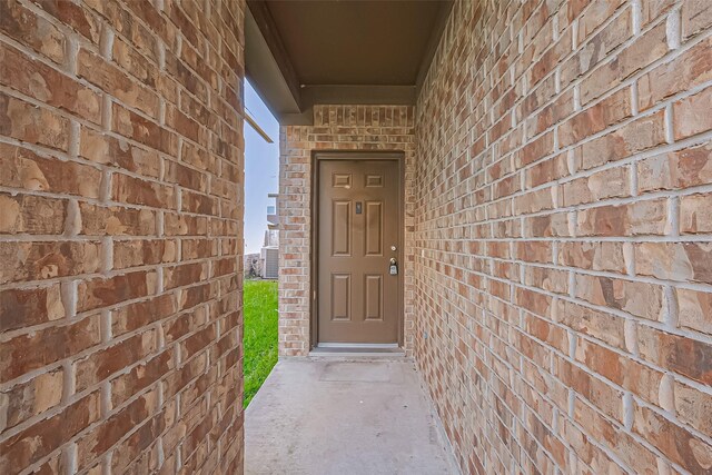 doorway to property featuring central AC and brick siding