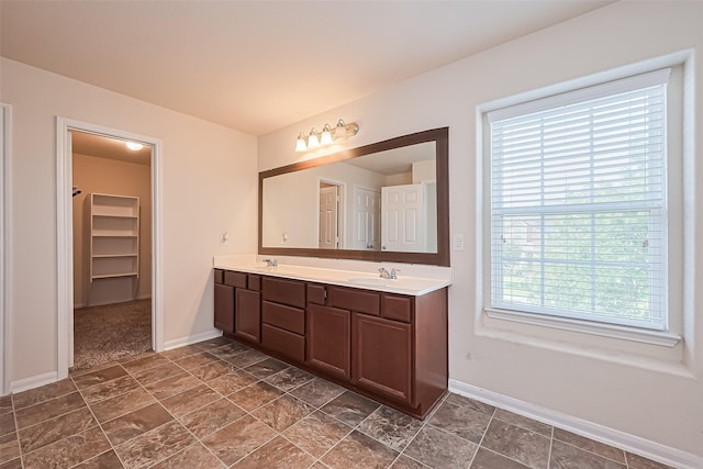 bathroom with a sink, baseboards, double vanity, and a spacious closet