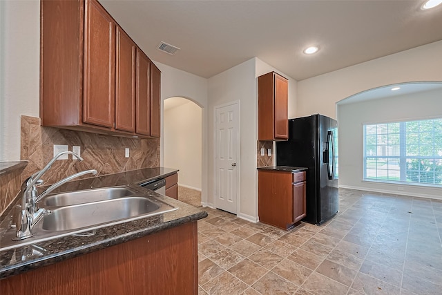 kitchen with dark countertops, a sink, arched walkways, visible vents, and black fridge with ice dispenser