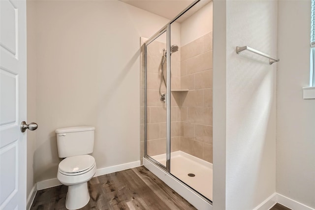 full bath with toilet, baseboards, wood finished floors, and a stall shower