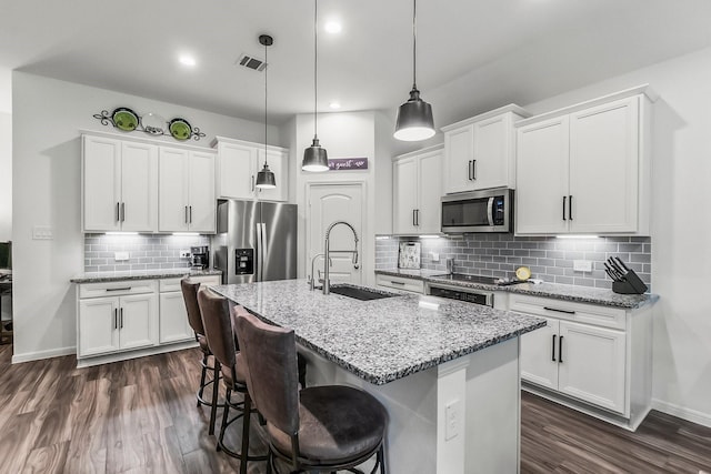 kitchen with a breakfast bar area, white cabinets, a sink, appliances with stainless steel finishes, and backsplash