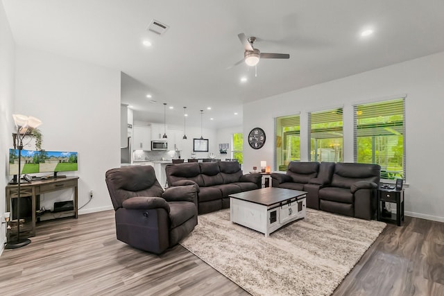 living area with visible vents, light wood-style floors, ceiling fan, and baseboards