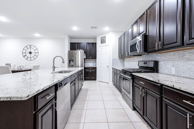 kitchen featuring tasteful backsplash, light stone counters, a sink, light tile patterned floors, and stainless steel appliances