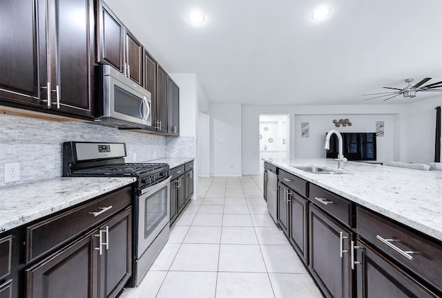 kitchen featuring backsplash, appliances with stainless steel finishes, a sink, light tile patterned floors, and light stone counters