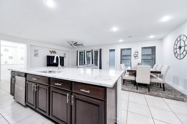 kitchen with stainless steel dishwasher, a sink, light tile patterned floors, light stone counters, and open floor plan
