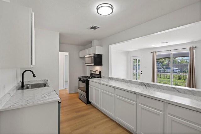 7817 Woodlyn Rd, Houston, TX 77028 - kitchen with appliances with stainless steel finishes, a sink, white cabinets, light wood-style flooring, and light stone countertops