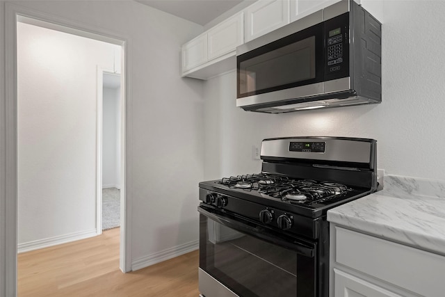 7817 Woodlyn Rd, Houston, TX 77028 - kitchen featuring black gas range oven, stainless steel microwave, light wood-type flooring, white cabinets, and baseboards