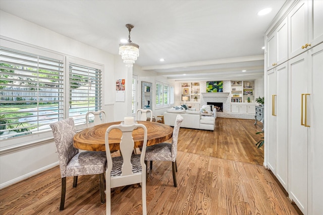 dining room with an inviting chandelier, light wood-style floors, a brick fireplace, and recessed lighting