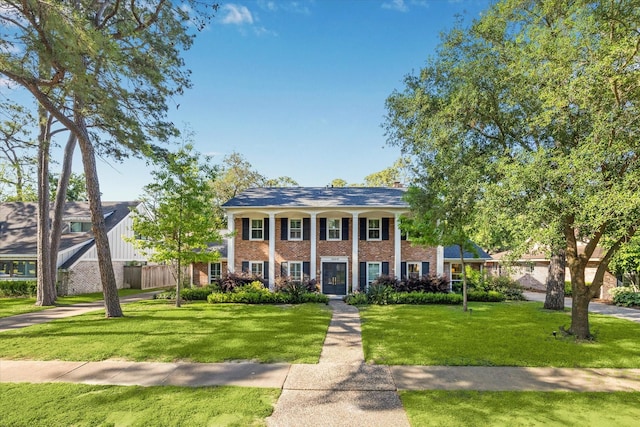 neoclassical / greek revival house with brick siding, fence, and a front yard