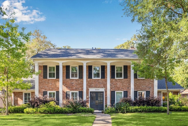 greek revival house with a chimney, a front lawn, and brick siding
