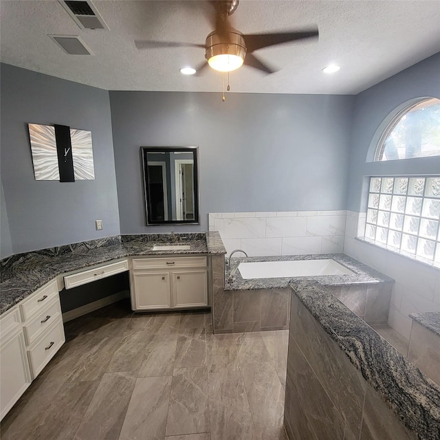 full bathroom featuring visible vents, vanity, a textured ceiling, a bath, and a ceiling fan