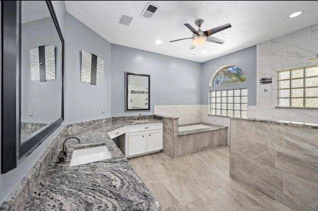 bathroom with ceiling fan, a garden tub, a textured ceiling, two vanities, and a sink