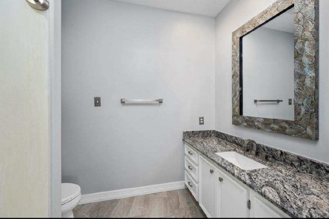 half bathroom featuring baseboards, toilet, and vanity