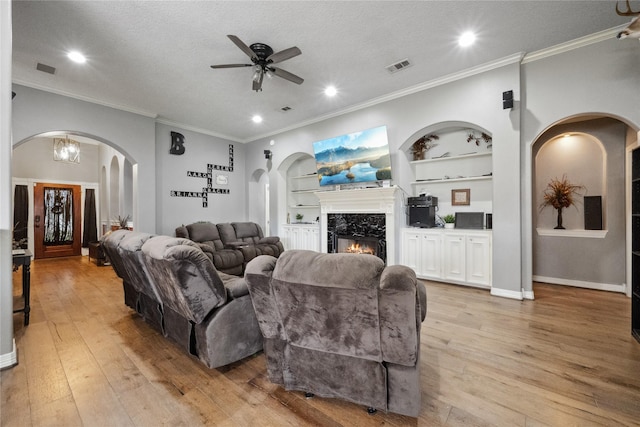 living room featuring arched walkways, built in features, a ceiling fan, light wood-type flooring, and visible vents