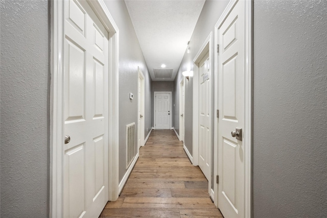 hallway with a textured wall, light wood finished floors, recessed lighting, baseboards, and visible vents