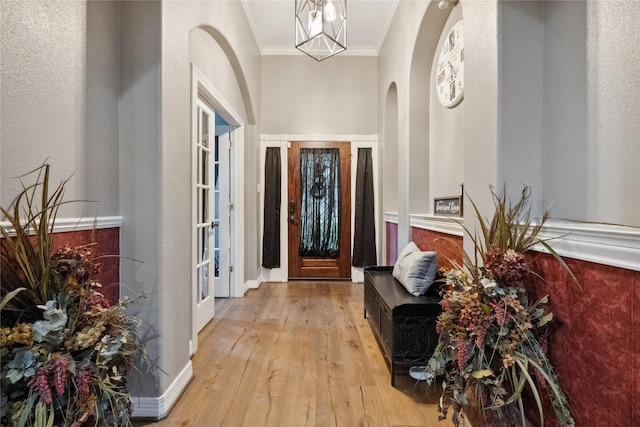 entryway with light wood-type flooring, arched walkways, a textured wall, and crown molding