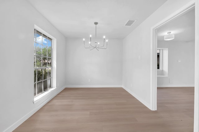 unfurnished dining area with visible vents, baseboards, a notable chandelier, and light wood-type flooring