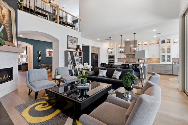 208 S Empress Green Pl, Montgomery, TX 77316 - living room featuring a towering ceiling, arched walkways, light wood-type flooring, a glass covered fireplace, and recessed lighting