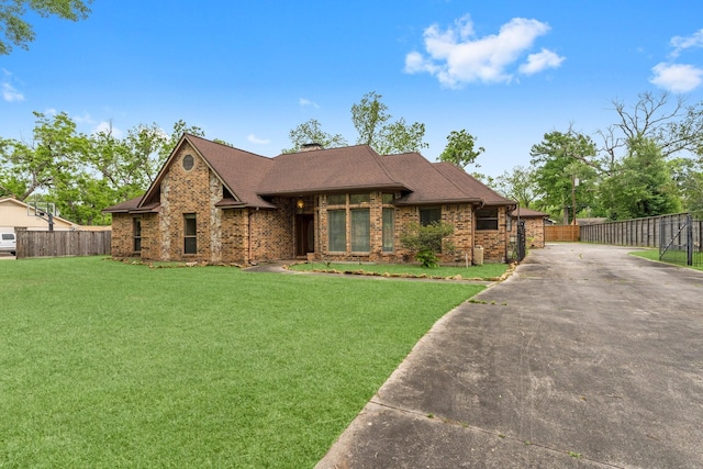 view of front facade with fence, brick siding, a front yard, a chimney, and driveway