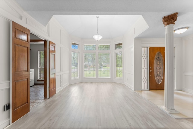 interior space with crown molding, decorative columns, a decorative wall, and light wood finished floors
