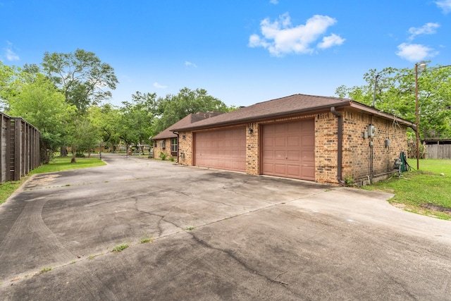 view of property exterior featuring brick siding, fence, and driveway
