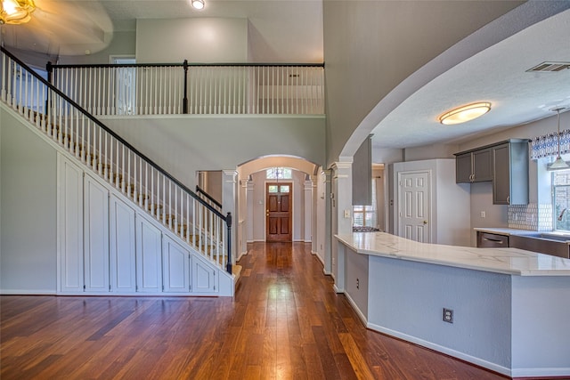 entryway featuring arched walkways, ornate columns, dark wood-style flooring, stairs, and a towering ceiling