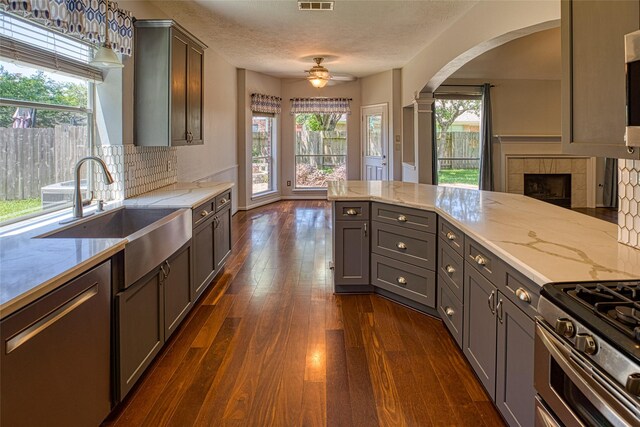 kitchen featuring a sink, arched walkways, ceiling fan, a tile fireplace, and appliances with stainless steel finishes