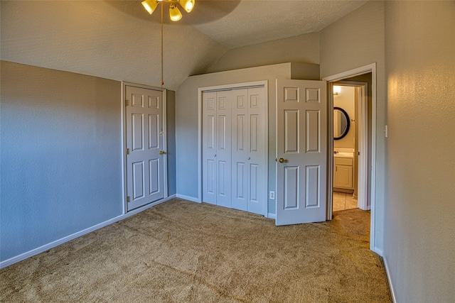 unfurnished bedroom with lofted ceiling, carpet floors, a closet, baseboards, and ceiling fan
