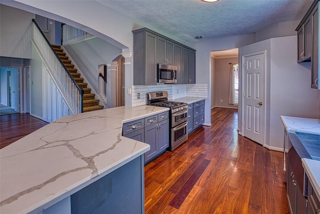 kitchen with appliances with stainless steel finishes, ornate columns, light stone countertops, dark wood finished floors, and decorative backsplash
