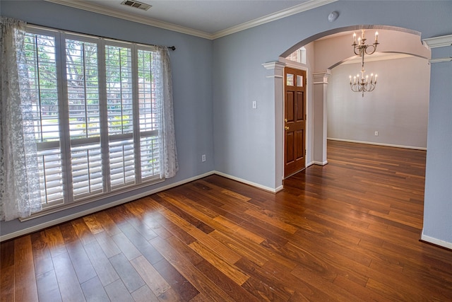 spare room featuring arched walkways, ornate columns, hardwood / wood-style floors, a chandelier, and ornamental molding